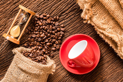 Directly above shot of roasted coffee beans with hourglass and coffee cup on wooden table