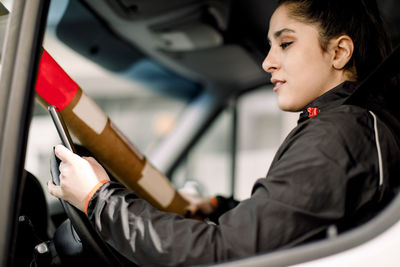 Young delivery woman using smart phone while driving truck