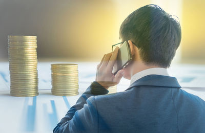 Double exposure of stacked coins and businessman answering smart phone