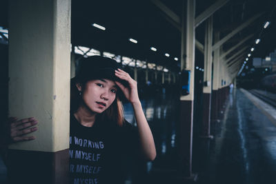 Portrait of young woman standing by pole at railroad station platform