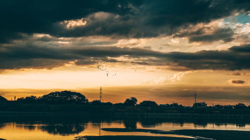 Silhouette trees by lake against sky during sunset