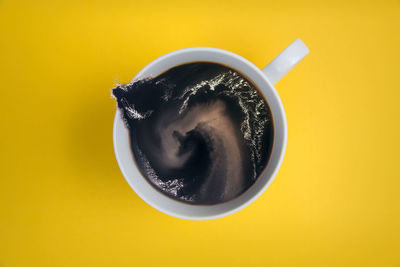 Directly above shot of black coffee splashing in cup over yellow background