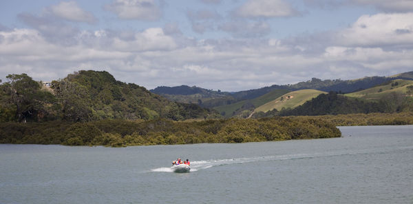 People riding boat on river by mountain against sky