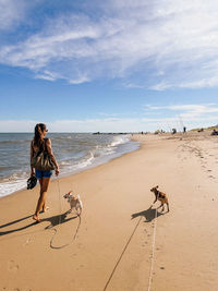 Rear view of woman walking at beach against sky
