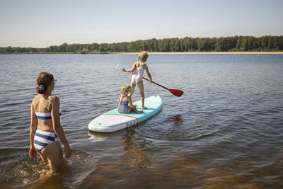 Girls having fun on paddleboard with mother at lake