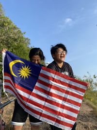Young women holding malaysian flag against sky