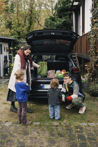 Father and mother talking to children near electric car outside house