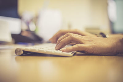 Cropped hands of female student typing on keyboard at desk