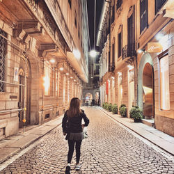 Rear view of woman standing on street amidst buildings in city