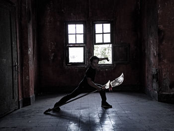 Full length of man holding blade while standing against window