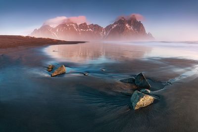 Scenic view of sea by snowcapped mountain against sky during winter