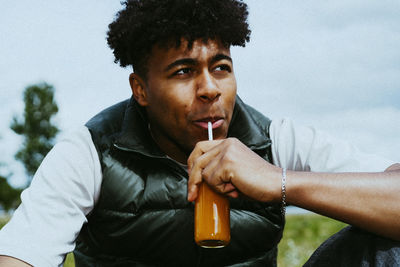 Young man drinking juice from bottle while looking away
