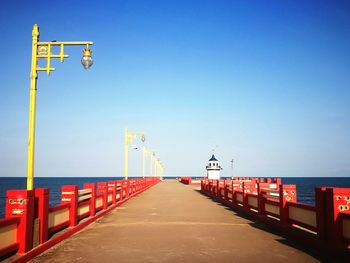 Empty road by sea against clear blue sky