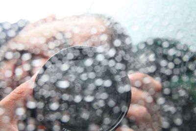 Close-up of person photographing with camera seen through wet car window