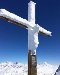 Cross on snow covered mountain against blue sky