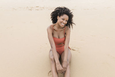 Happy beautiful young woman sitting on sand at beach
