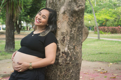 Happy young woman touching tree trunk