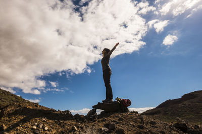 Low angle view of woman standing with arms outstretched on land against sky