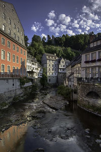 Arch bridge over river amidst buildings in city against sky