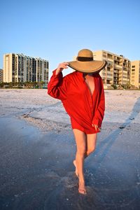 Mature woman wearing hat standing at beach against clear sky