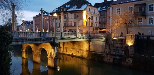 Illuminated bridge over river by buildings in city at night
