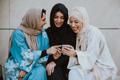 Young woman using smart phone while sitting on laptop