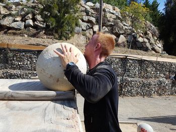 Side view of man lifting stone sphere