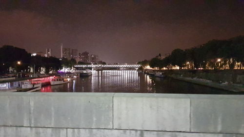 Illuminated buildings by river against sky at night