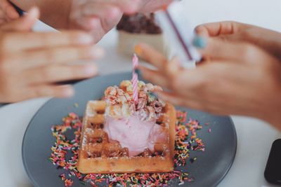 Cropped hands of people by waffle in plate on table
