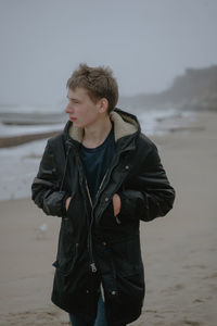 A guy in a winter jacket walks along the beach, grinds to the side, a teenager travels
