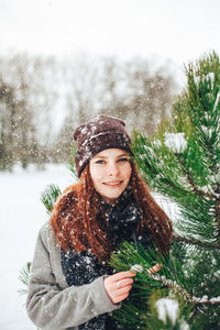 Portrait of smiling young woman standing by tree in winter