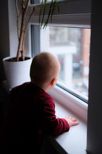 Rear view of boy looking through window