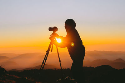 Silhouette man photographing against sky during sunset