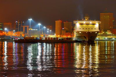 Illuminated buildings by river against sky at night