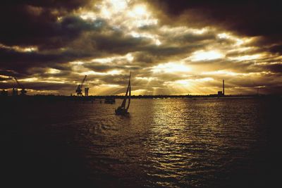 Silhouette of sailboats in sea against cloudy sky