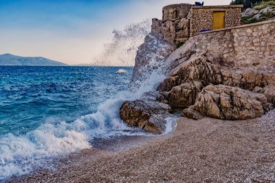 Waves splashing on rocks at shore against sky