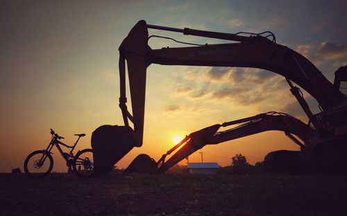 Silhouette construction site on field against sky during sunset