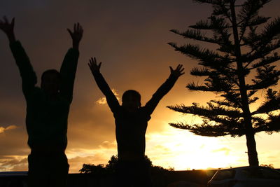 Silhouette people standing by tree against sky during sunset