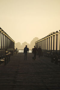 People walking on footbridge against clear sky