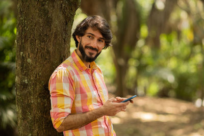 Young man with smartphone at day time with a green park in the background. mobile phone, technology,