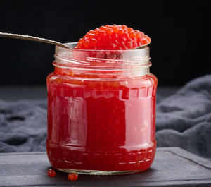 Fresh grainy red caviar in a glass jar on a wooden table