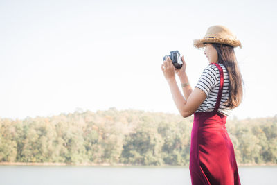 Woman photographing while standing against clear sky