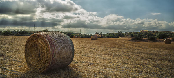 Hay bales on field against cloudy sky