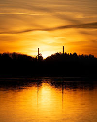 Silhouette trees by lake against orange sky