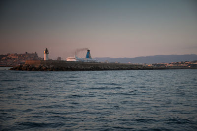 Lighthouse by sea against clear sky during sunset