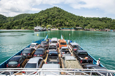 Cars on ferry at river against mountain