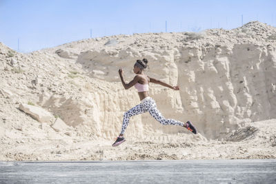 Side view of female athlete running on road against rock formation during sunny day