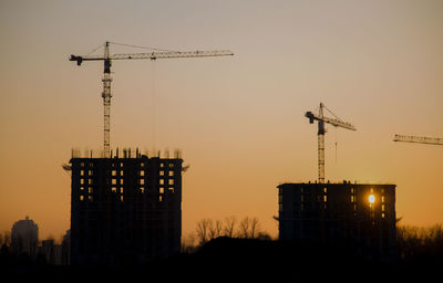 Silhouette crane by building against sky during sunset