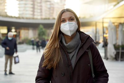 Woman wearing medical face mask in city street as prevention against virus looking at camera