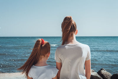 Rear view of female friends standing at beach against clear sky